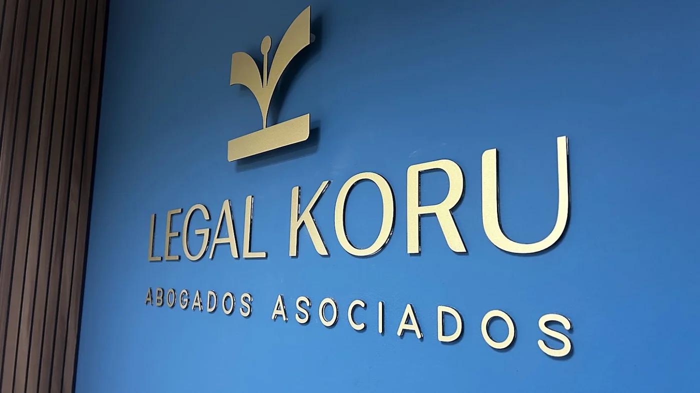 Logotipo corpóreo en acrílico dorado sobre muro azul corporativo de Legal Koru